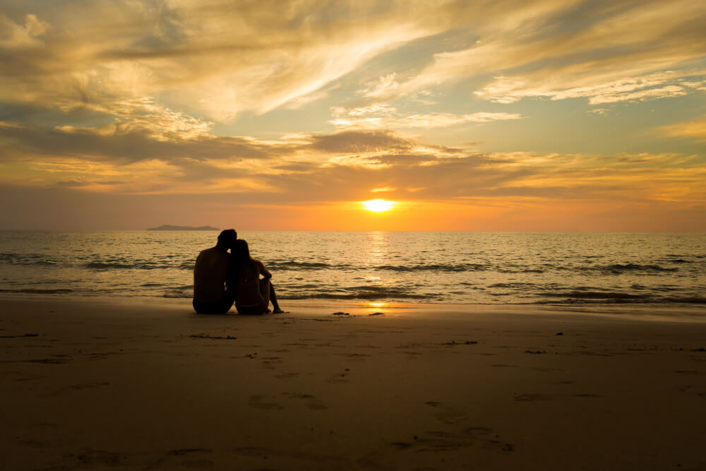 A couple watching the sunset on a beach during their romantic getaway to the Outer Banks.